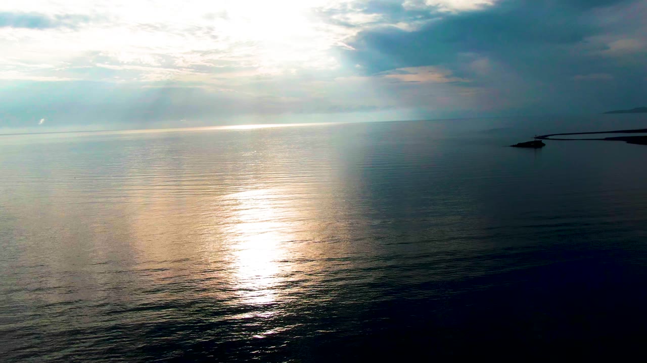 Sunlight glints across calm ocean water near Santa Rosalia, Baja California Sur, with layered clouds over the horizon and no visible people.