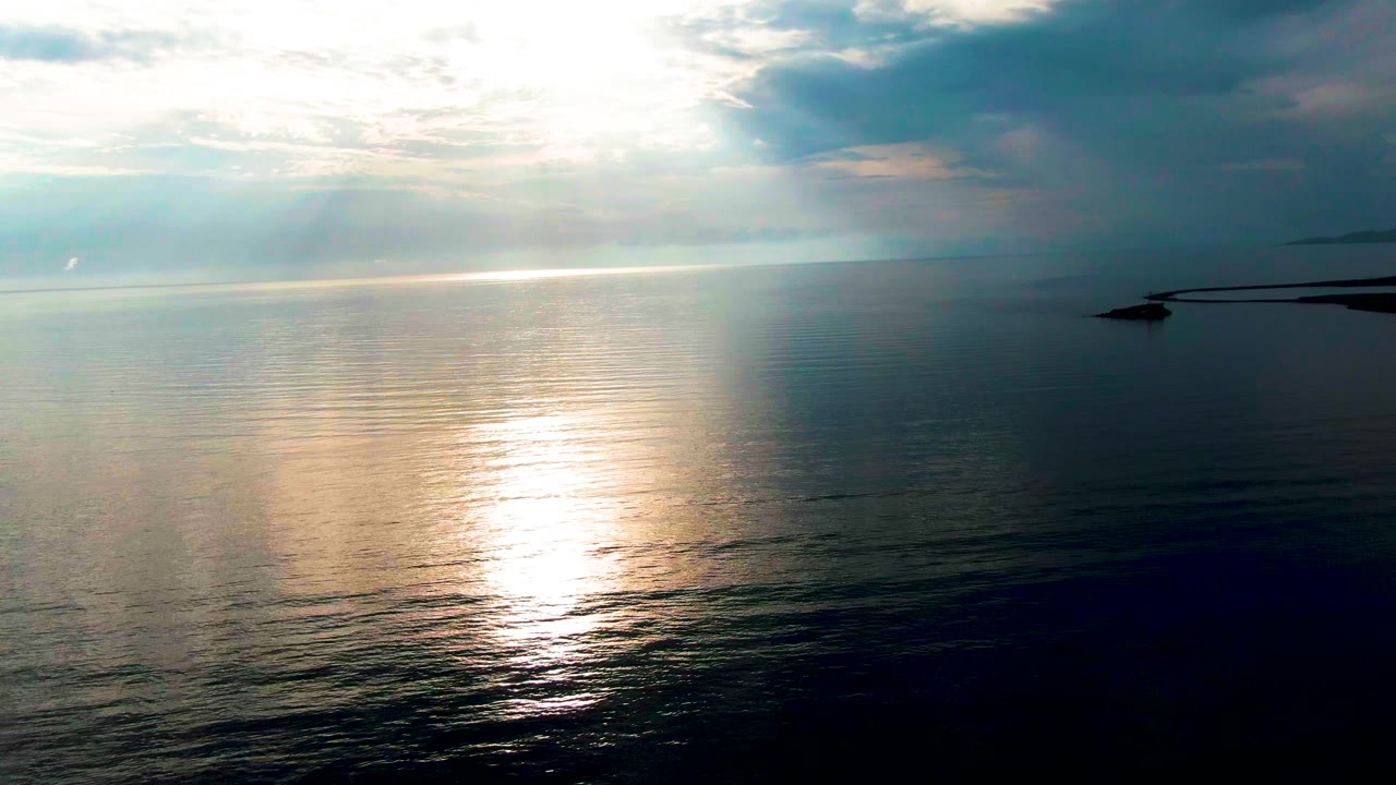A bright vertical glare reflects on the Santa Rosalia ocean surface while darker cloud mass shades the right side of the frame, with no visible people.