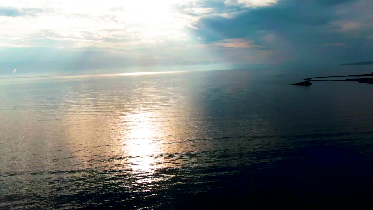 Gold light spreads over blue ocean near Santa Rosalia as a dark shoreline shape remains at the right edge beneath a clouded sky, with no visible people.