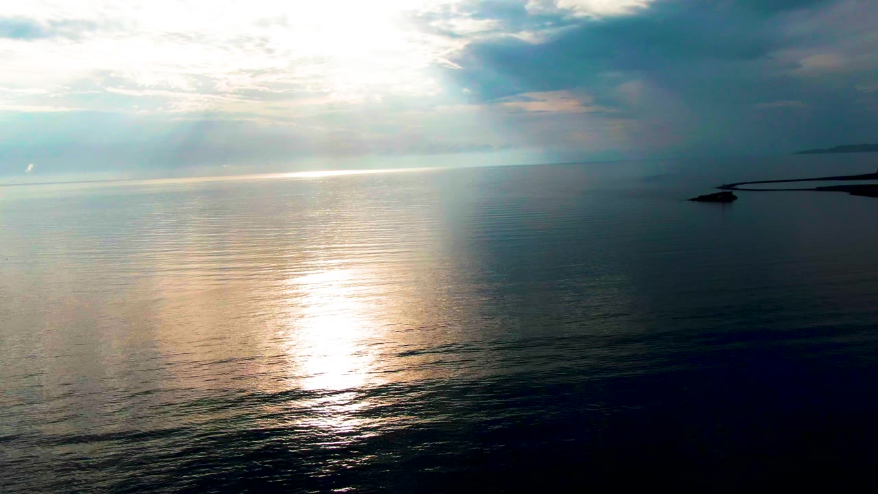 Calm sea with sun reflection and pale clouds