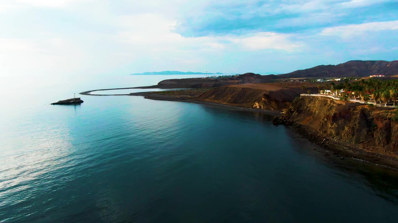 Aerial view of calm ocean beside a rocky coastal cliff and shore road.