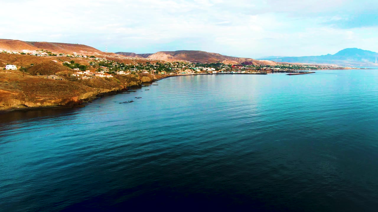 Calm turquoise water beside a rocky coast with hillside buildings.
