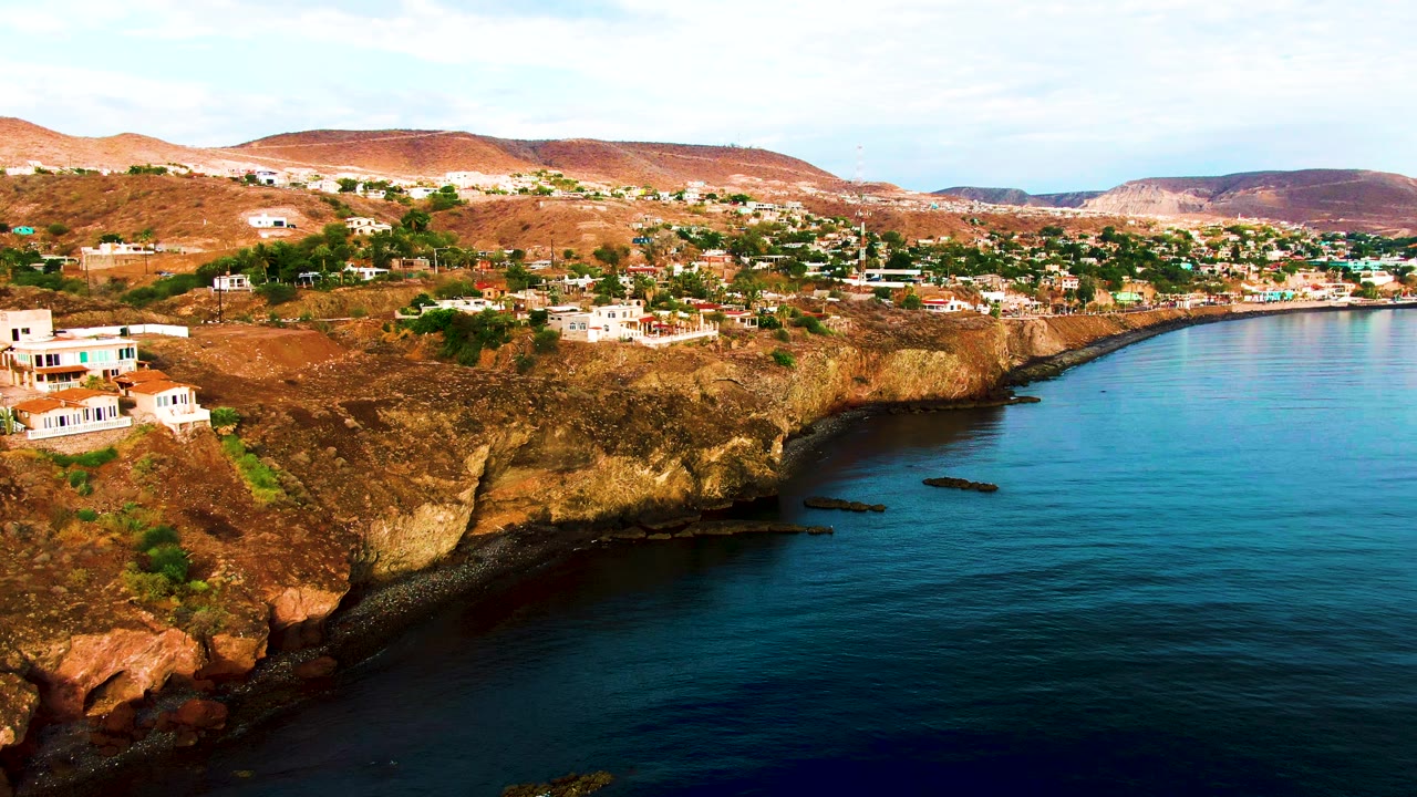 White houses on arid cliffs above a sheltered blue shoreline