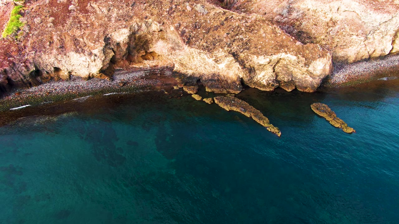 Overhead rocky shoreline with turquoise water and a small bird at left.