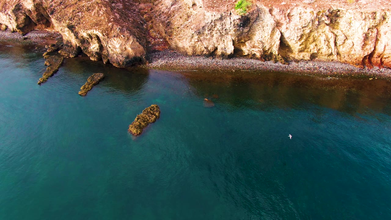 Aerial view of Santa Rosalia cliffs and blue-green water with a small white object visible over the water near the right side and no visible people.