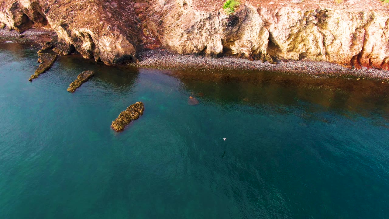 Cliff shoreline with offshore rocks and clear water.