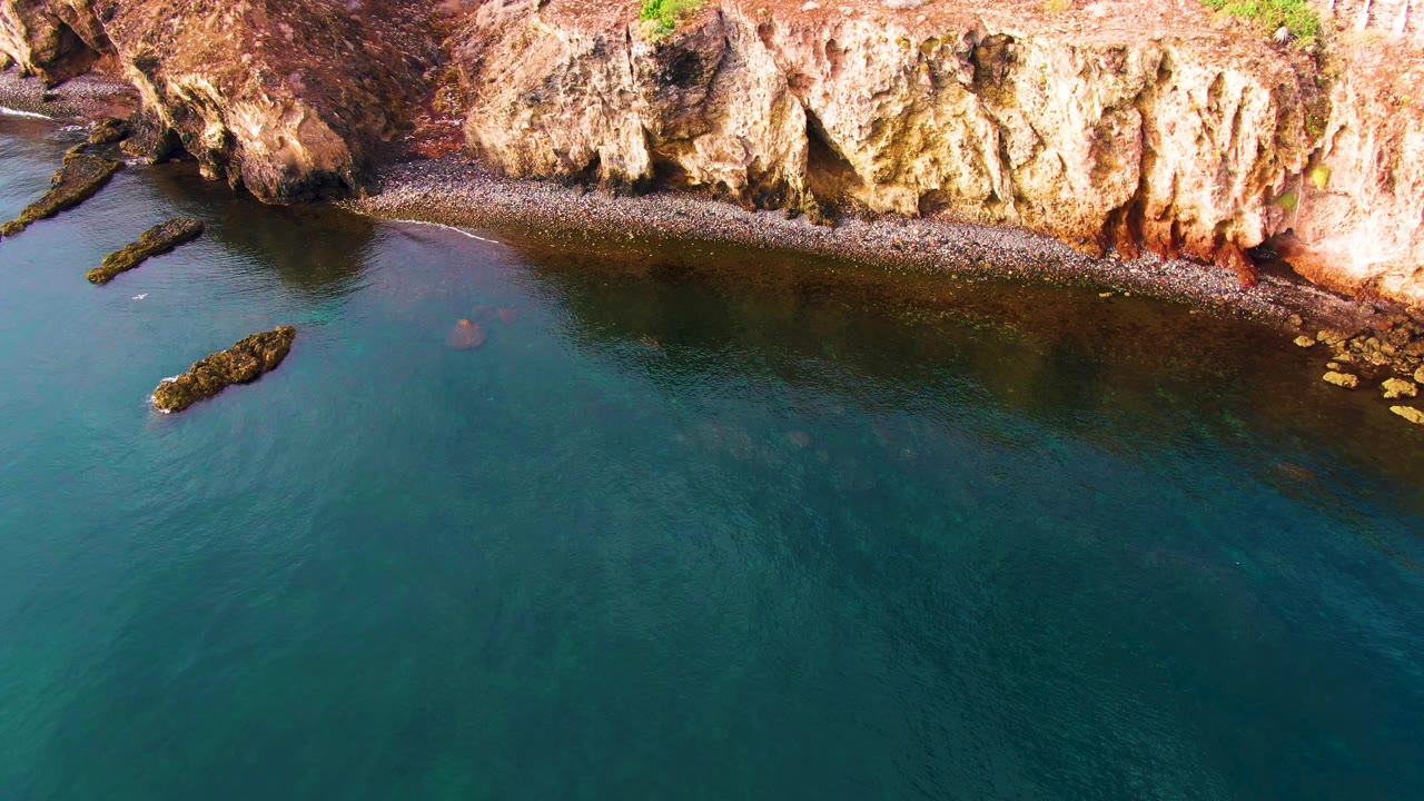 Aerial view of blue-green water beside a rocky shoreline.