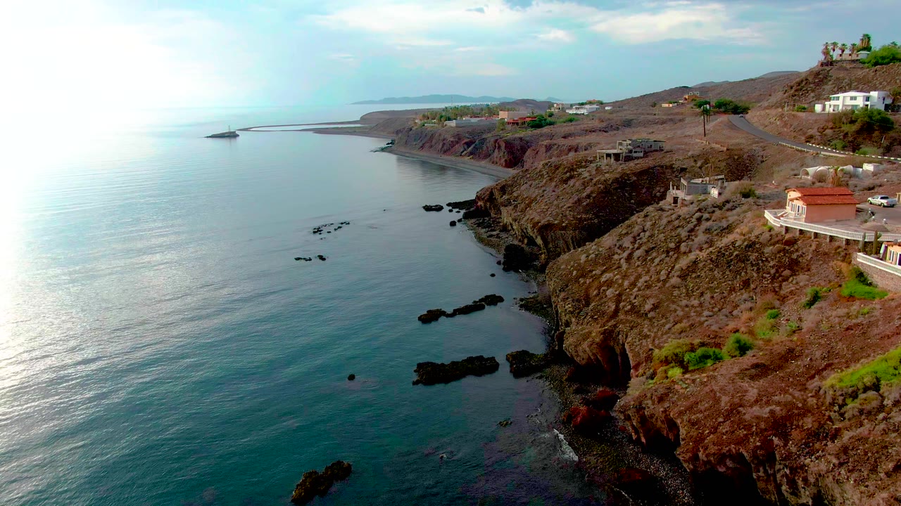 Rocky shoreline with ocean reflection and scattered buildings on the cliff.
