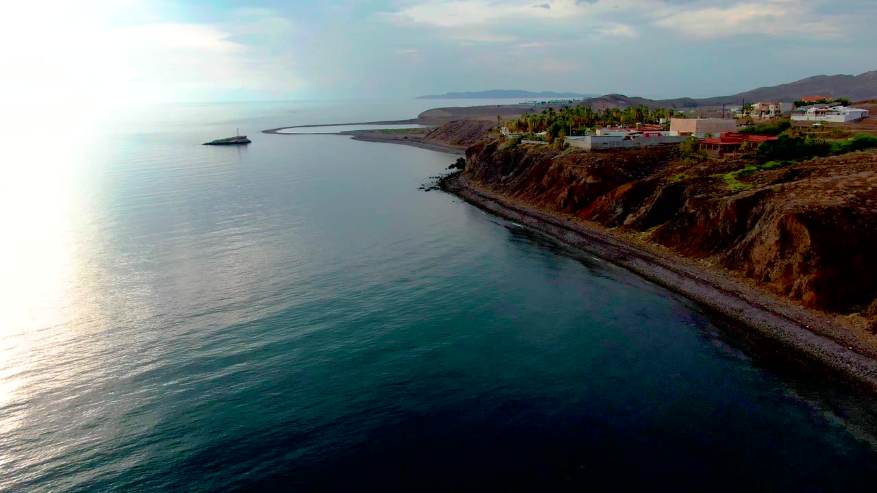 Aerial coastal view with stronger view of the bluff, shoreline, and buildings under cloudy sky.