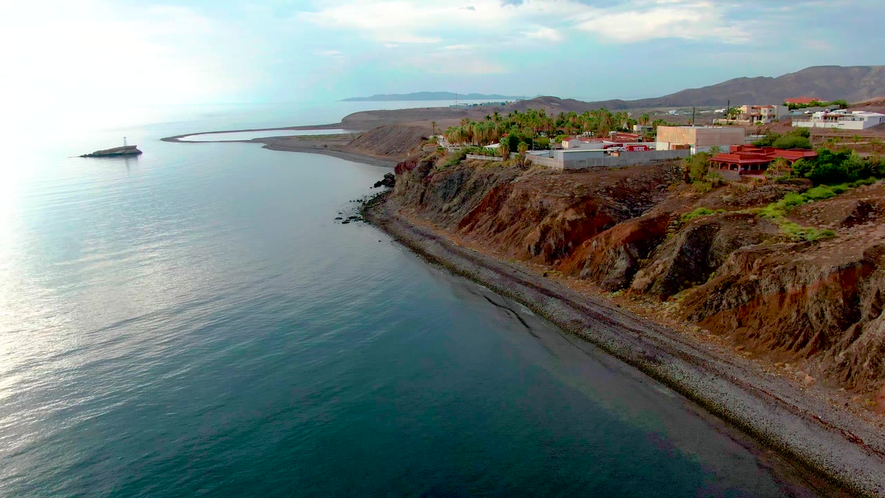 Aerial coastline view with sunlit water and rocky bluff.