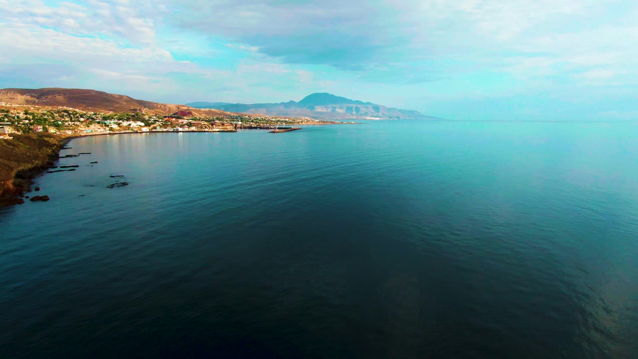 Santa Rosalia coastline seen from above with dark rocks along the left edge, scattered buildings on the shore, broad rippled water, and no visible people.