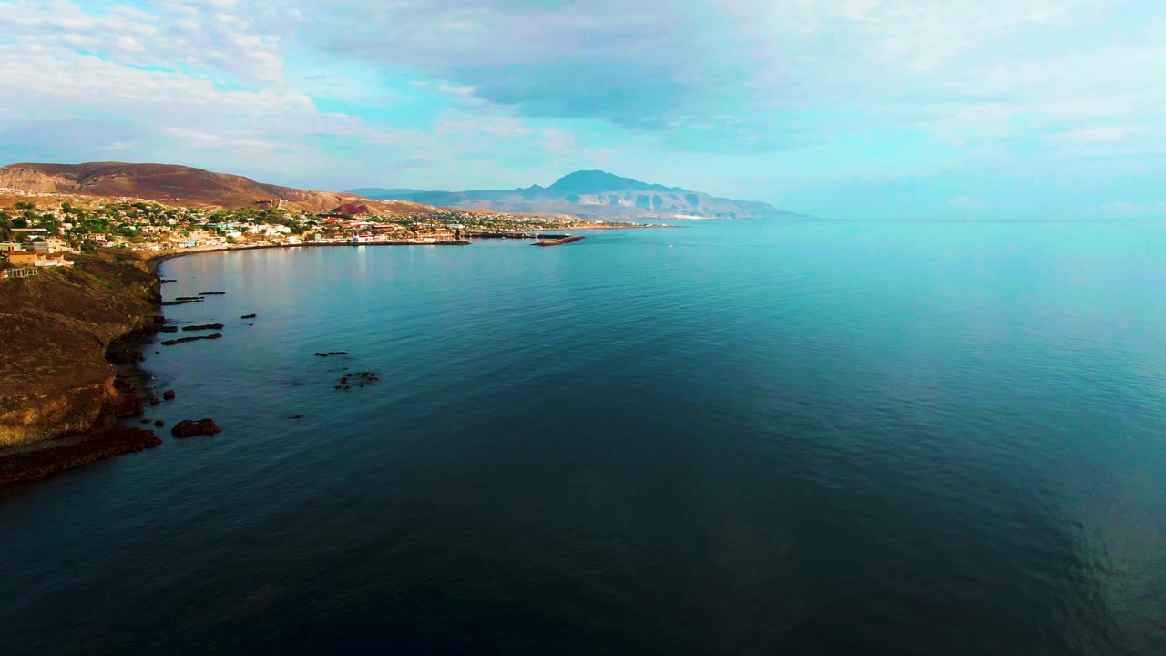 Rocky shoreline curves beside open water with buildings in the distance.