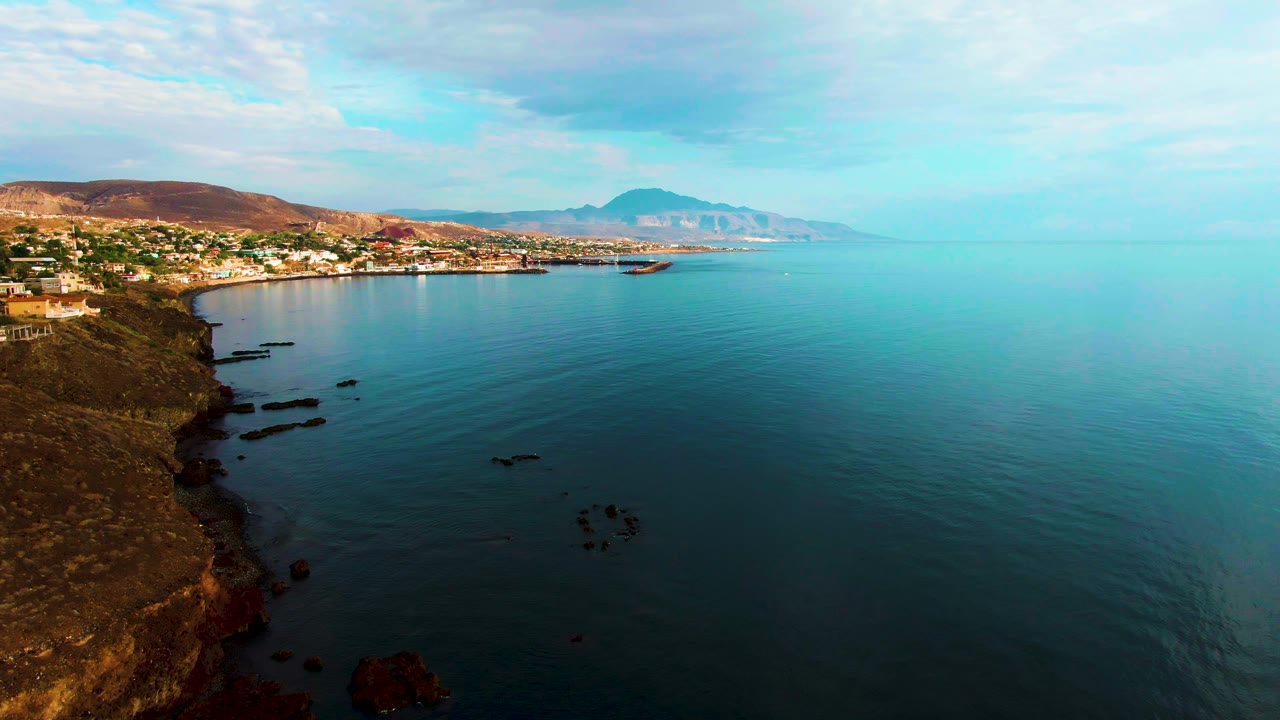 Rocky coastal bluff with calm bay water and town in the distance.