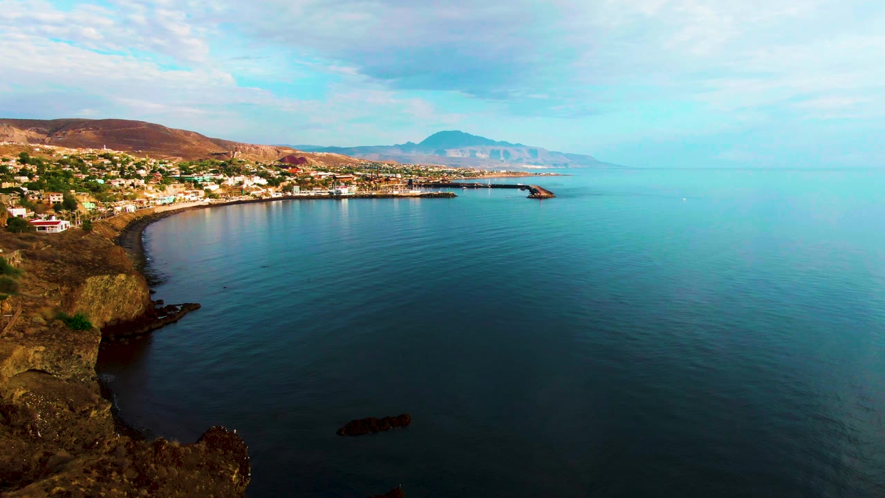 Coastal buildings and rocky cliffs beside a calm bay.