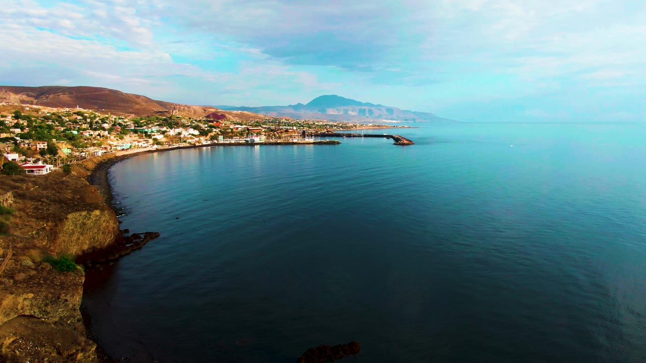 Curved rocky bay with coastal town and calm ocean surface.