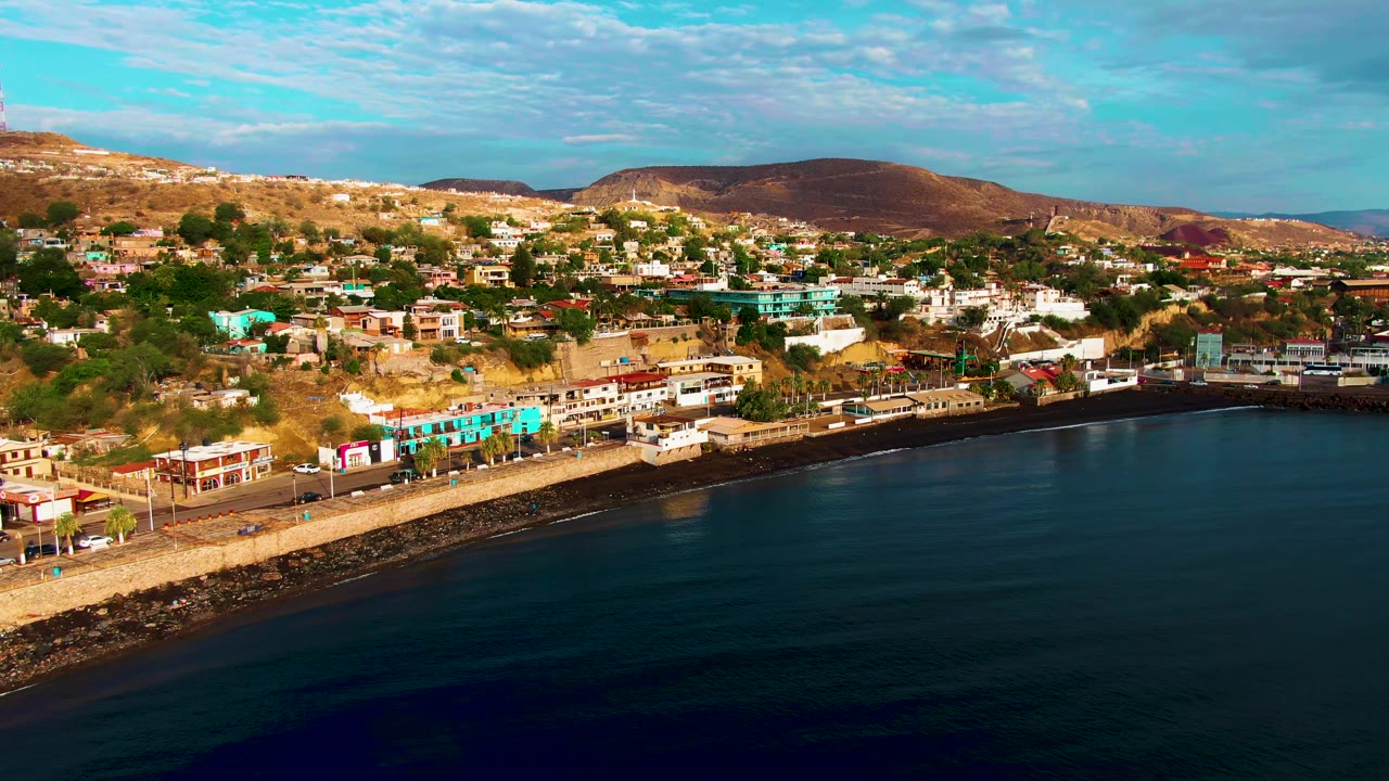 Aerial shoreline view with ocean foreground, highway traffic, and town buildings.