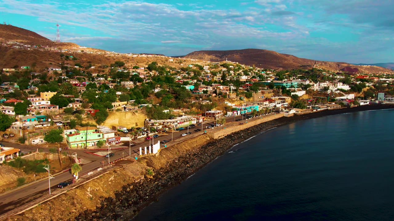 Elevated view of a coastal road, hillside town, and bay water.