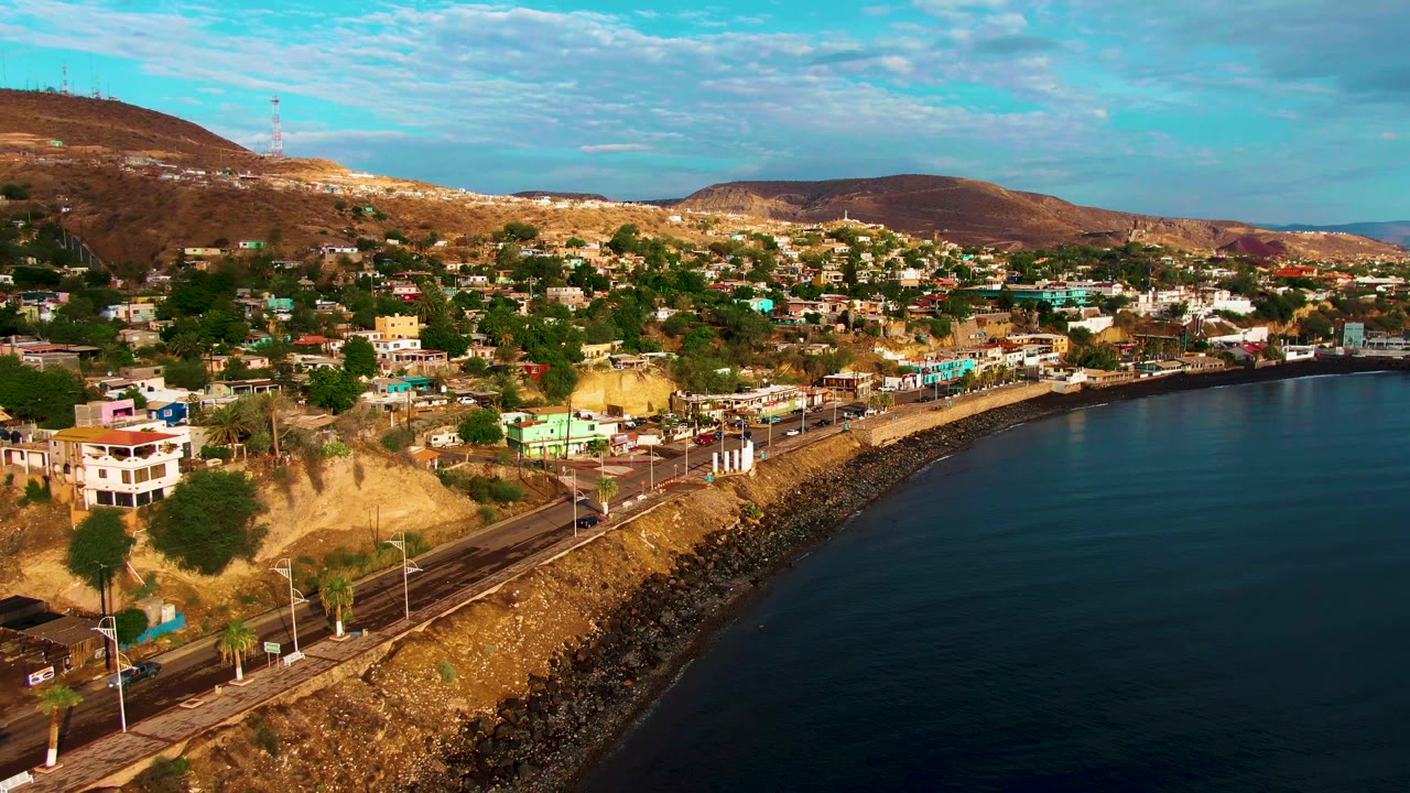 Aerial shoreline view with a white building near the road and hills behind town.