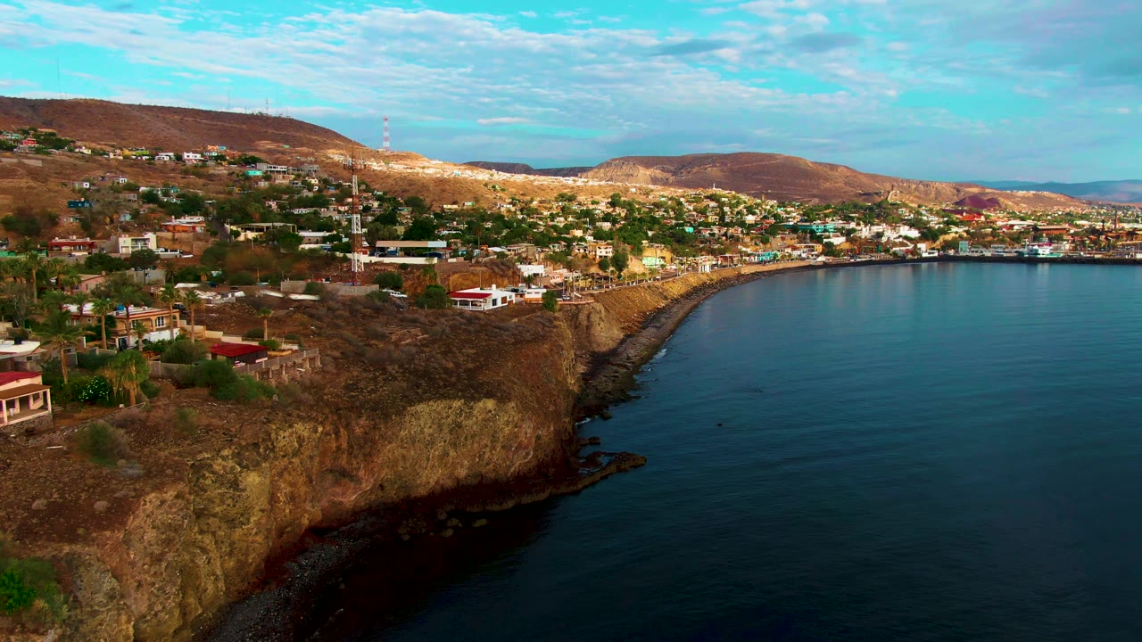 Rocky coastal bluff with houses, a tower, and calm water beside the town.