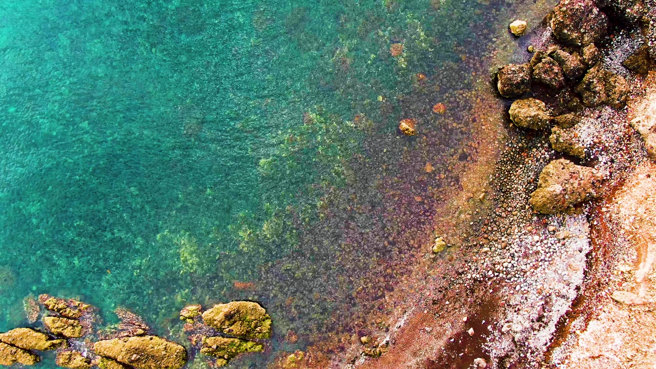Clear green-blue water washes over rocks beside a sandy edge.