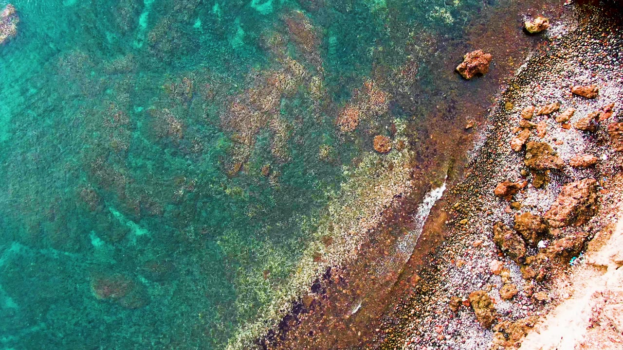 Rocky shore and shallow blue-green water from above.