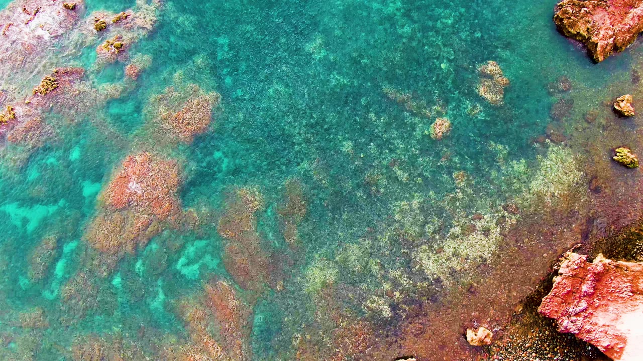 Turquoise water over reddish submerged rocks and shallow seabed