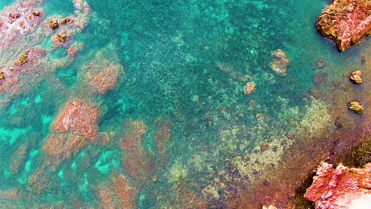 Clear green-blue water in Santa Rosalia shows submerged reddish and tan rocks under gentle ripple patterns, with no visible people or boats.