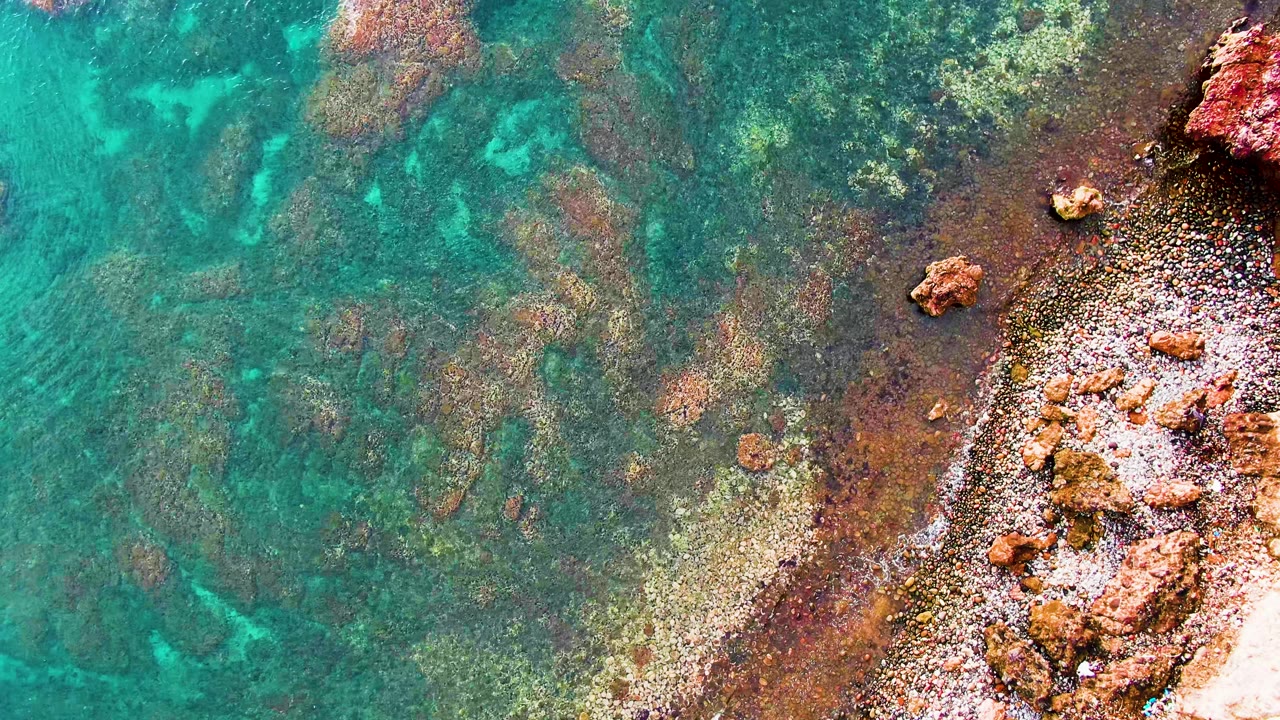 Turquoise shallow water beside reddish rocky shoreline