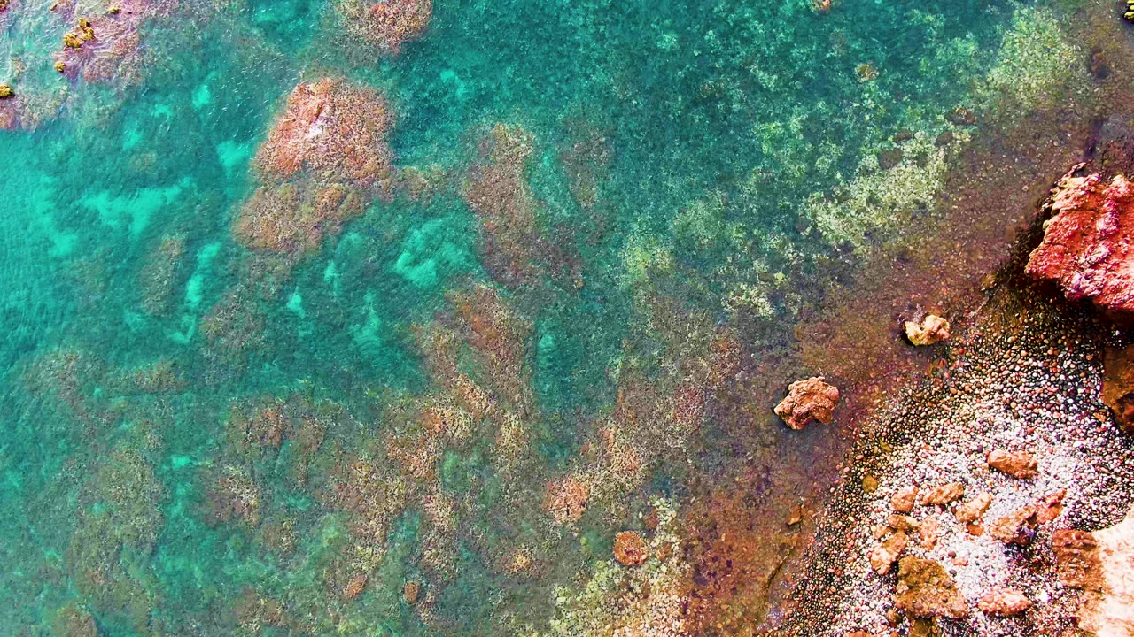 Turquoise water moves across shallow rock formations with a bright pale edge near the lower right shoreline in Santa Rosalia, Mexico, with no visible people.
