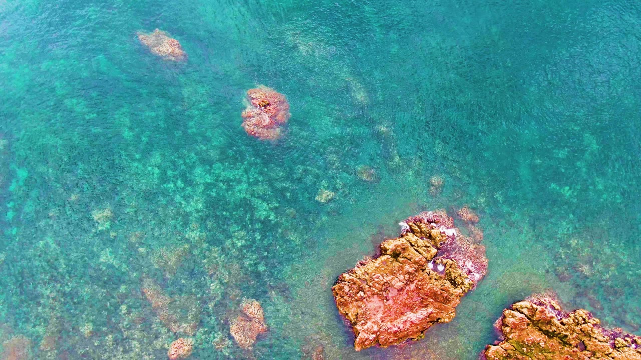 Shallow turquoise water with a large reddish rock near the lower center