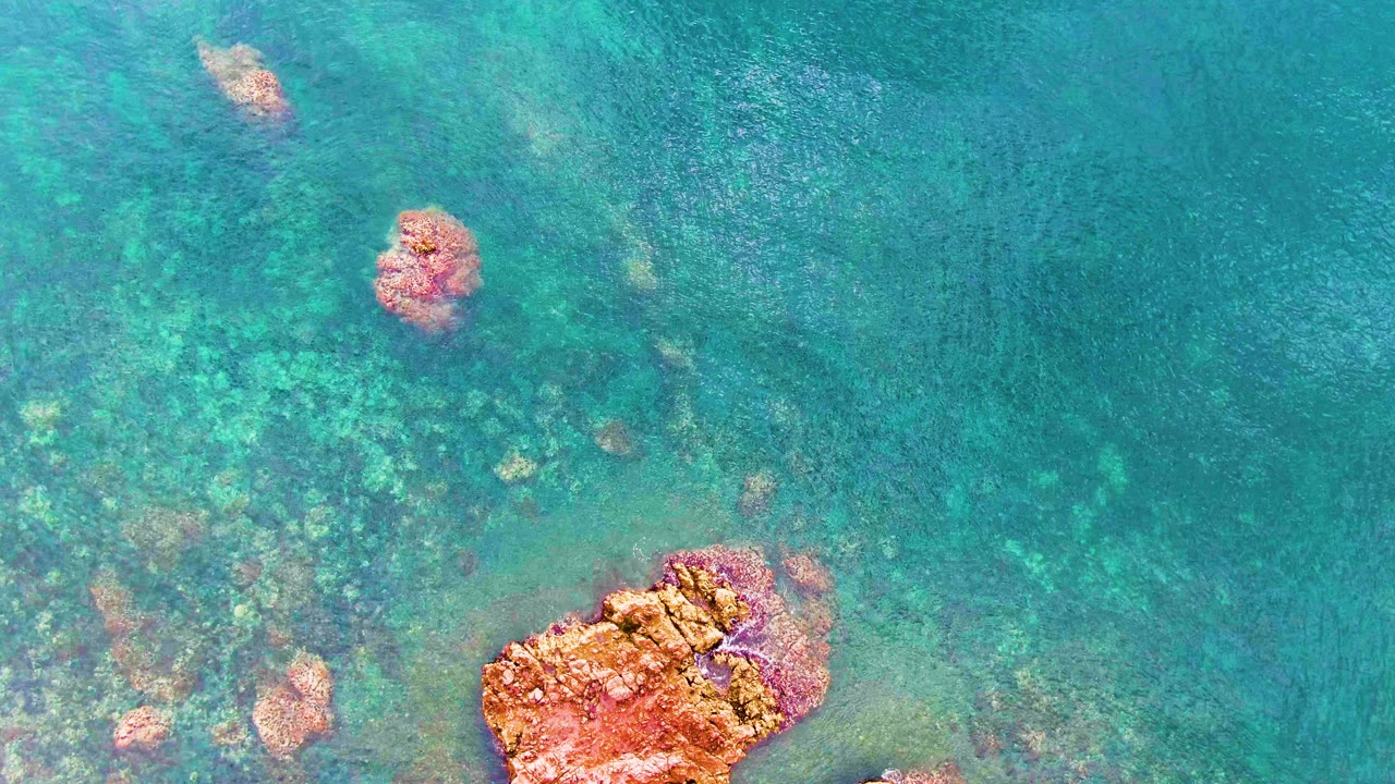Rippling turquoise ocean with submerged rocks and a large rock at the bottom.