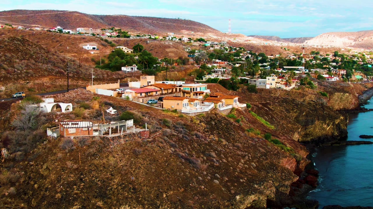 Aerial view in Santa Rosalia, Baja California Sur, showing dry hillside homes above a rocky ocean edge with no visible people.