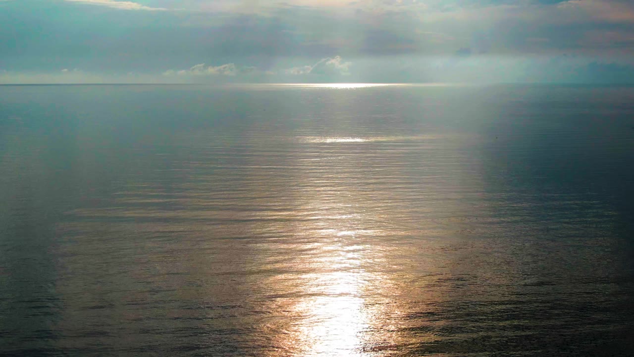 Sunlight reflecting on a calm ocean beneath clouds
