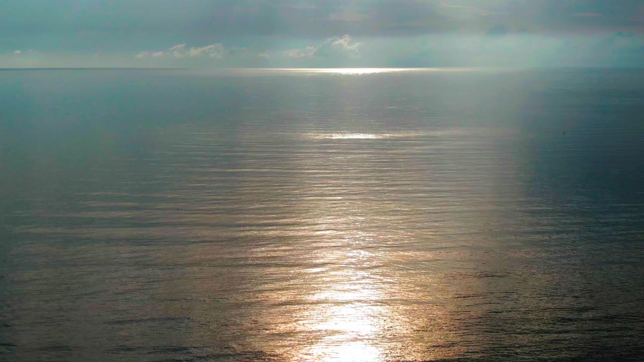 The sun reflection remains centered on calm water off Santa Rosalia, Mexico, while the overcast sky darkens the surrounding sea and no people are visible.