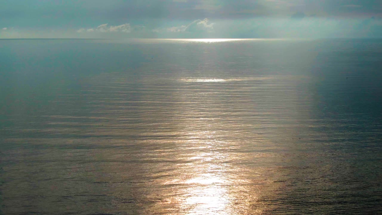 Soft sunlight reflects across rippled ocean water near Santa Rosalia, Mexico, with a darker cloud band at the horizon and no visible people.
