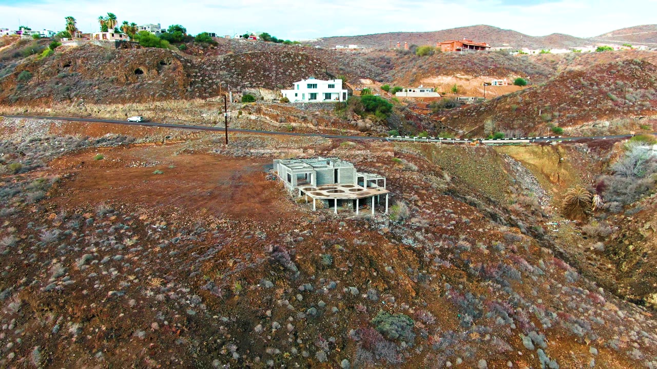 Opening frame of Santa Rosalia, Baja California Sur, with a white car on the road, a concrete structure below, houses across the hillside, and no visible people.