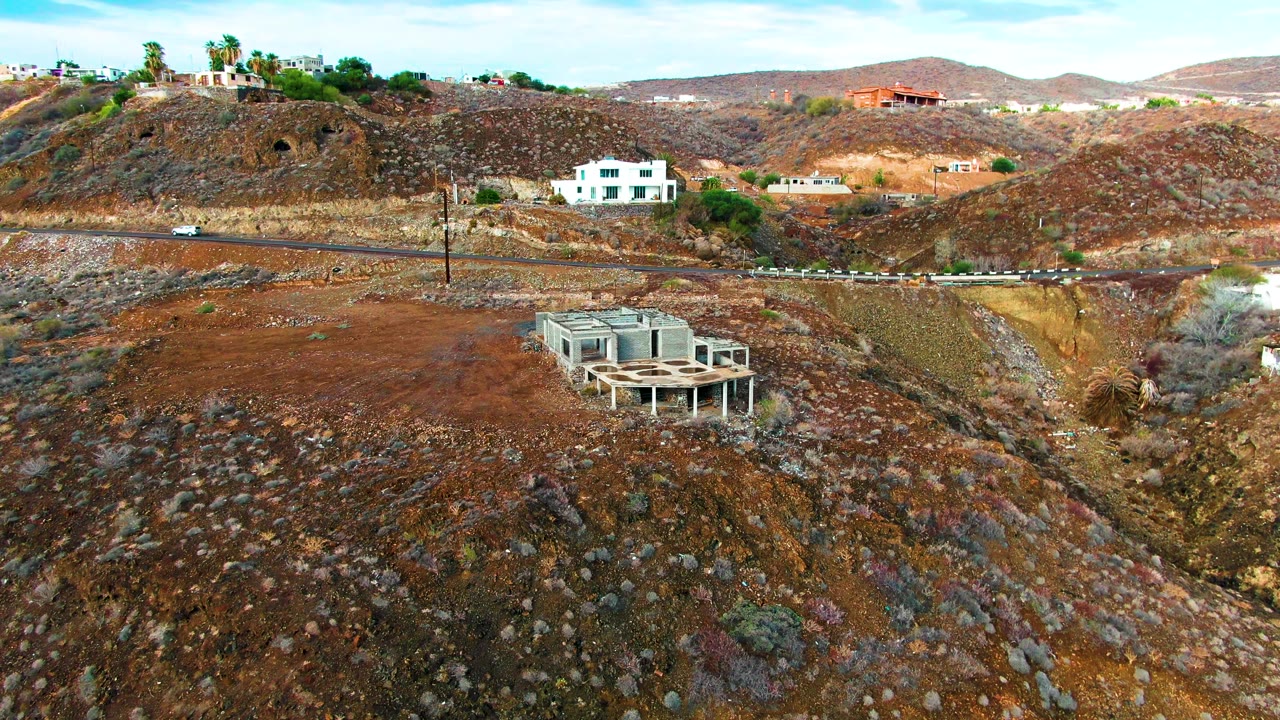Hillside road and dry rocky slope with houses and a concrete structure.