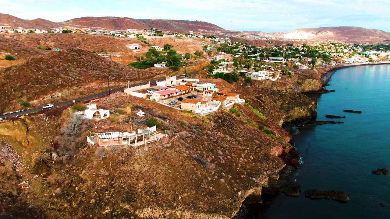 Aerial view of hillside homes beside a road and curved shoreline.