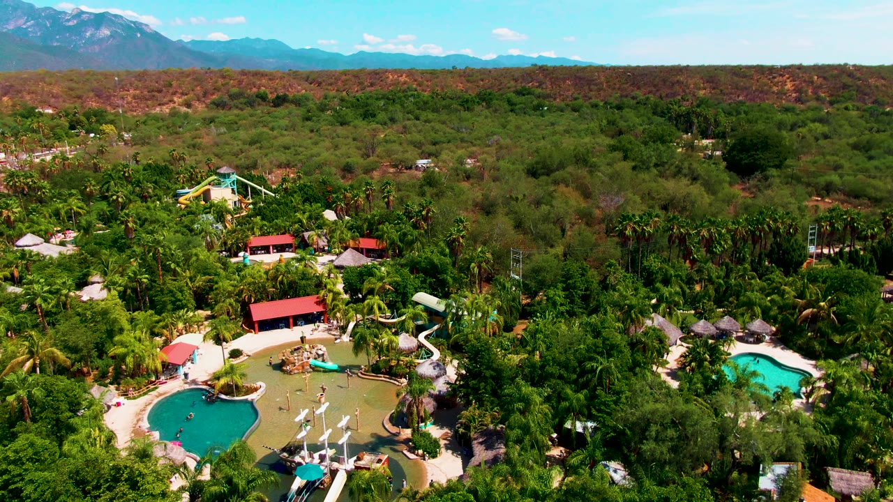 Aerial view of resort pools surrounded by dense trees and distant mountains