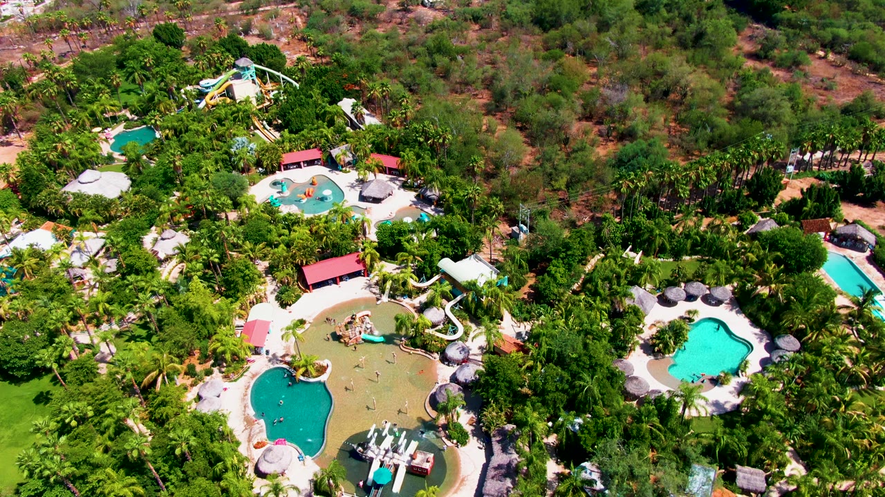 Aerial view of a resort water slide, pools, umbrellas, and trees.