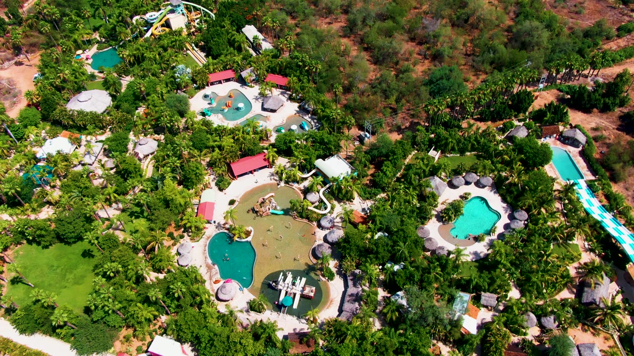Drone view of a resort pool area with water slides and thick trees.