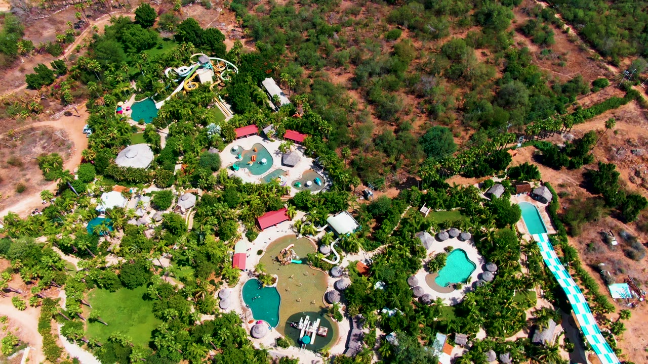 Drone view of pools and slides surrounded by palms and scrubland.