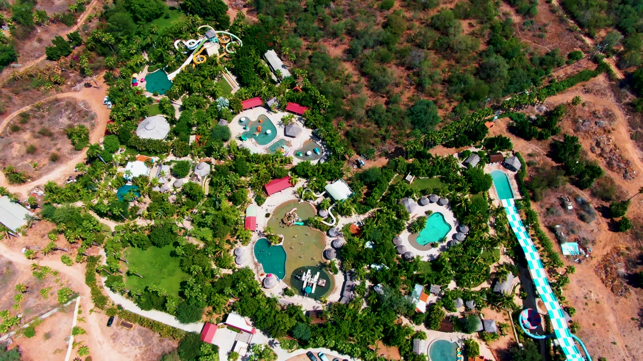 Overhead frame in Caduano, Baja California Sur showing the water park slightly farther across the grounds, with curved pools, a long slide on the right, parking near the bottom, and no visible people.