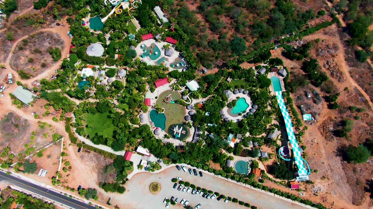 Water park from above with green landscaping, pool shapes, parked cars, and road beside dry land.