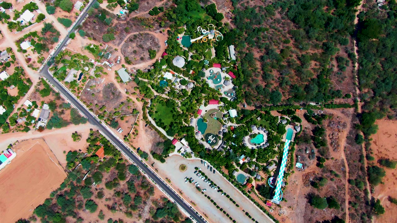Aerial view of pools and greenery with a car moving along the road.