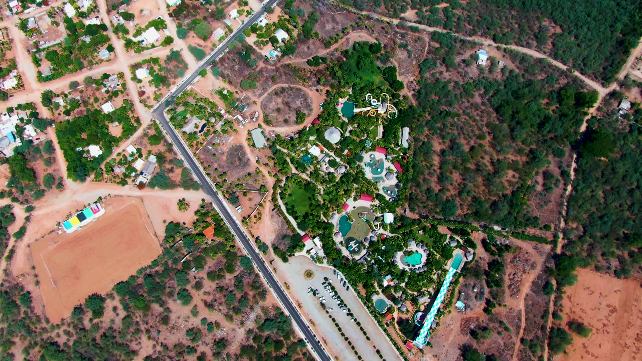 Drone view of vehicles on a road near homes, pools, and dense greenery.