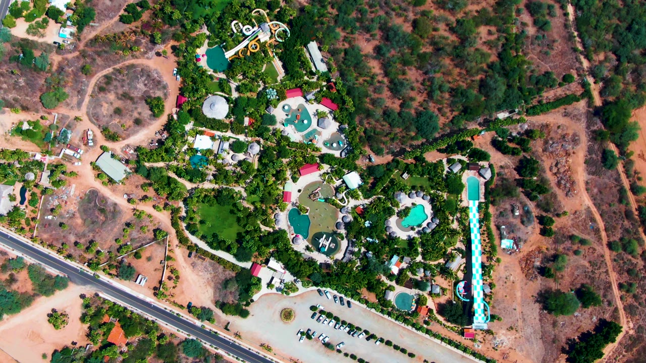 Aerial view of resort pools and slides beside a parking area and scrub-covered hills.