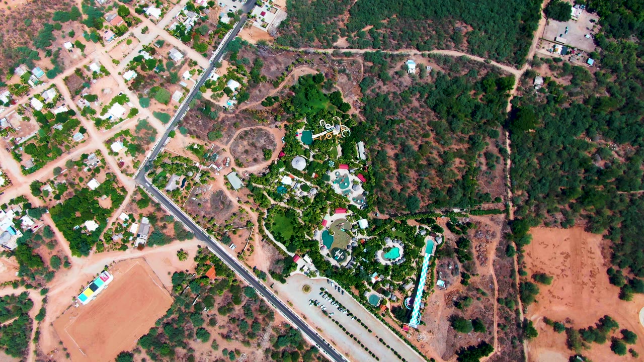 Top-down frame of road, residential lots, green trees, and resort pools.