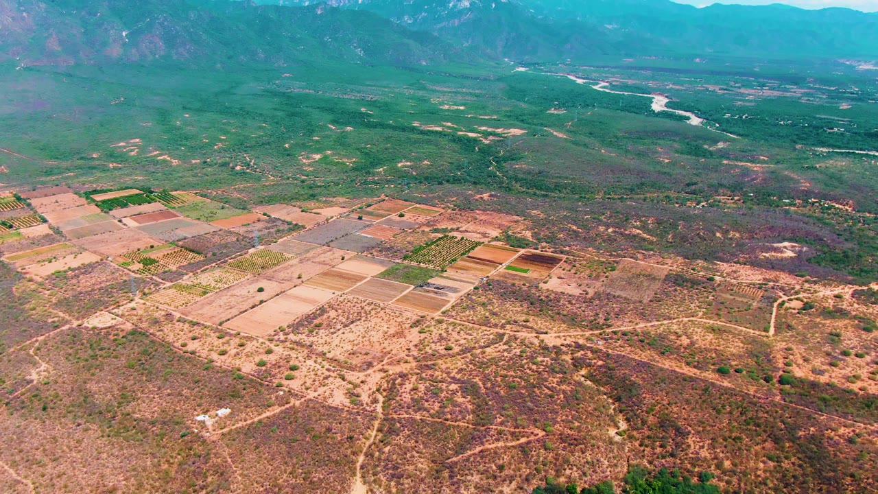 Aerial view of dry farmland, green fields, mountains, and river in the distance.