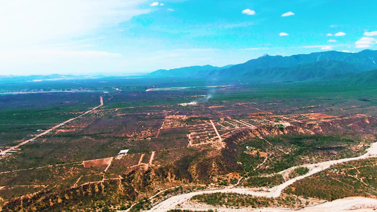 High view over dry wash, farmland patches, roads, and distant blue mountains.